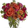 Bouquet of orange roses and purple daisies in a clear glass vase
