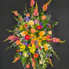 Tall standing spray of yellow lilies, orange roses, and bright mixed flowers on a black background