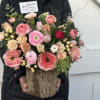 Mixed pink and peach flowers arranged in a rustic wood container