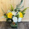 Yellow roses and white flowers in a glass vase with greenery