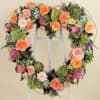 Heart-shaped floral wreath with roses and succulents on a stand