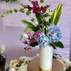 Tall floral arrangement with blue hydrangeas and magenta orchids in a white vase