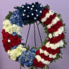 Circular floral wreath in red, white, and blue with star accents on a stand