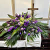 Purple and green floral casket spray with a crucifix behind it