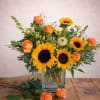 Sunflowers and orange roses arranged in a clear glass vase