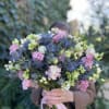 Handheld bouquet of pink, white, and blue flowers tied with a ribbon