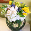 Bouquet of white roses, yellow tulips, and blue flowers in a round glass vase