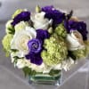 Bouquet of white roses, purple lisianthus, and green hydrangeas in a glass vase