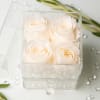 Four white roses in a clear acrylic box with scattered crystals