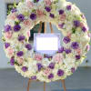 Large floral wreath of pink, purple, and white blooms on an easel with a blank sign
