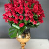 Red rose bouquet in a gold vase with large green leaves
