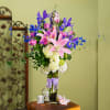 Tall bouquet of pink lilies, roses, and blue irises in a glass vase