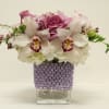 Pink roses and white orchids in a clear square vase with a purple wrap