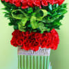 Tall arrangement of red roses with a green ribbon in a decorative pedestal vase