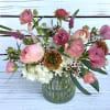 Small glass vase with pink ranunculus and mixed flowers in a loose, airy arrangement