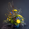 Tall floral arrangement with yellow chrysanthemums and blue flowers in a blue vase