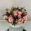 Low arrangement of pink roses with small purple blooms in a white ceramic vase