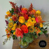 Vibrant arrangement of orange and yellow roses with yellow mums in a clear glass vase