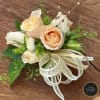 Peach rose corsage with white accents, gold ribbon bow, and jeweled pins on a wooden surface.