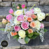 Pastel roses and ranunculus arranged in a white ceramic vase.