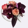 Compact bouquet of peach roses and purple orchids in a clear vase