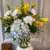 Yellow lilies and white daisies with blue hydrangea in a glass vase
