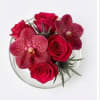 Red roses and spotted orchids arranged in a clear round vase