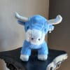 Blue plush bull toy with silver horns standing on a dark shelf