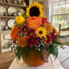 Autumn floral arrangement in a pumpkin-shaped container with sunflowers, roses, and mums