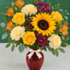 Yellow roses, sunflowers, and carnations in a red glass vase with a ribbon