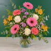 Pink gerbera daisies, white roses, and mixed blooms in a clear glass vase