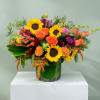 Bright mixed bouquet with sunflowers, roses, and purple blooms in a glass vase