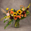 Mixed bouquet with sunflowers, roses, and orange blooms in a glass vase
