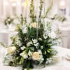White floral centerpiece with roses and lilies around tall candles