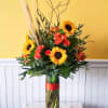 Sunflower and rose arrangement in a tall glass vase with a red ribbon