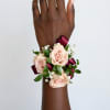 Peach rose wrist corsage with burgundy ribbon on a wrist