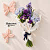Bouquet of purple, blue, and white flowers wrapped in white paper with black hearts