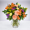 Mixed bouquet of orange, pink, yellow, and purple flowers in a glass vase