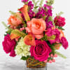 Bright mixed bouquet in a clear square vase with roses, calla lilies, and purple blooms
