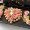 Pink roses and chocolates arranged in a black gift box with butterfly decorations.