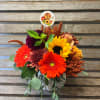 Fall bouquet with sunflowers, gerbera daisies, and a pumpkin pick in a white vase