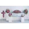 Pink and purple funeral floral arrangements around a silver casket