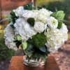 White floral arrangement in a clear glass vase with green accents