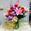 Mixed bouquet of pink lilies, red roses, and purple flowers in a glass vase