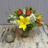 Bouquet of yellow lilies, orange roses, and white flowers in a glass vase