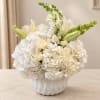 White floral arrangement in a white ceramic vase with lilies and hydrangeas