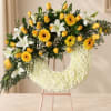 Yellow roses, white lilies, and gerbera daisies on a white floral wreath