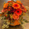 Orange and burgundy floral arrangement in a pumpkin container