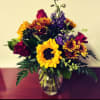 Bouquet of sunflowers, purple flowers, and red roses in a glass vase