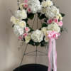 White and pink floral wreath on a stand with a pink ribbon